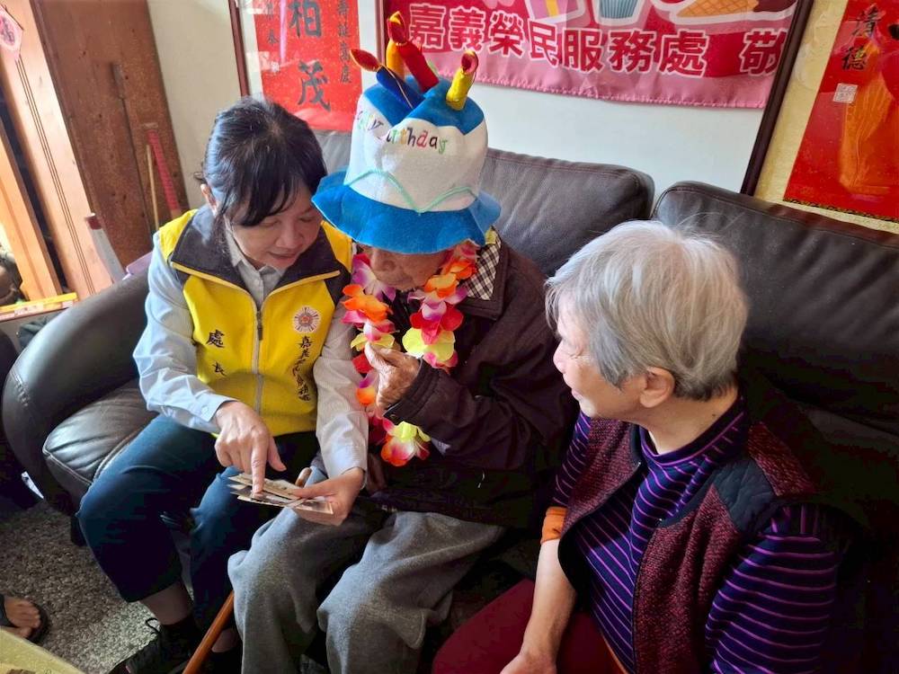 許淑菁處長率隊為百歲榮民何永忠伯伯歡喜賀壽，同時轉贈總統賴清德、行政院長卓榮泰的賀壽壽屏，及退輔會嚴德發主任委員賀壽金飾及蛋糕。（圖/嘉義榮服處提供）