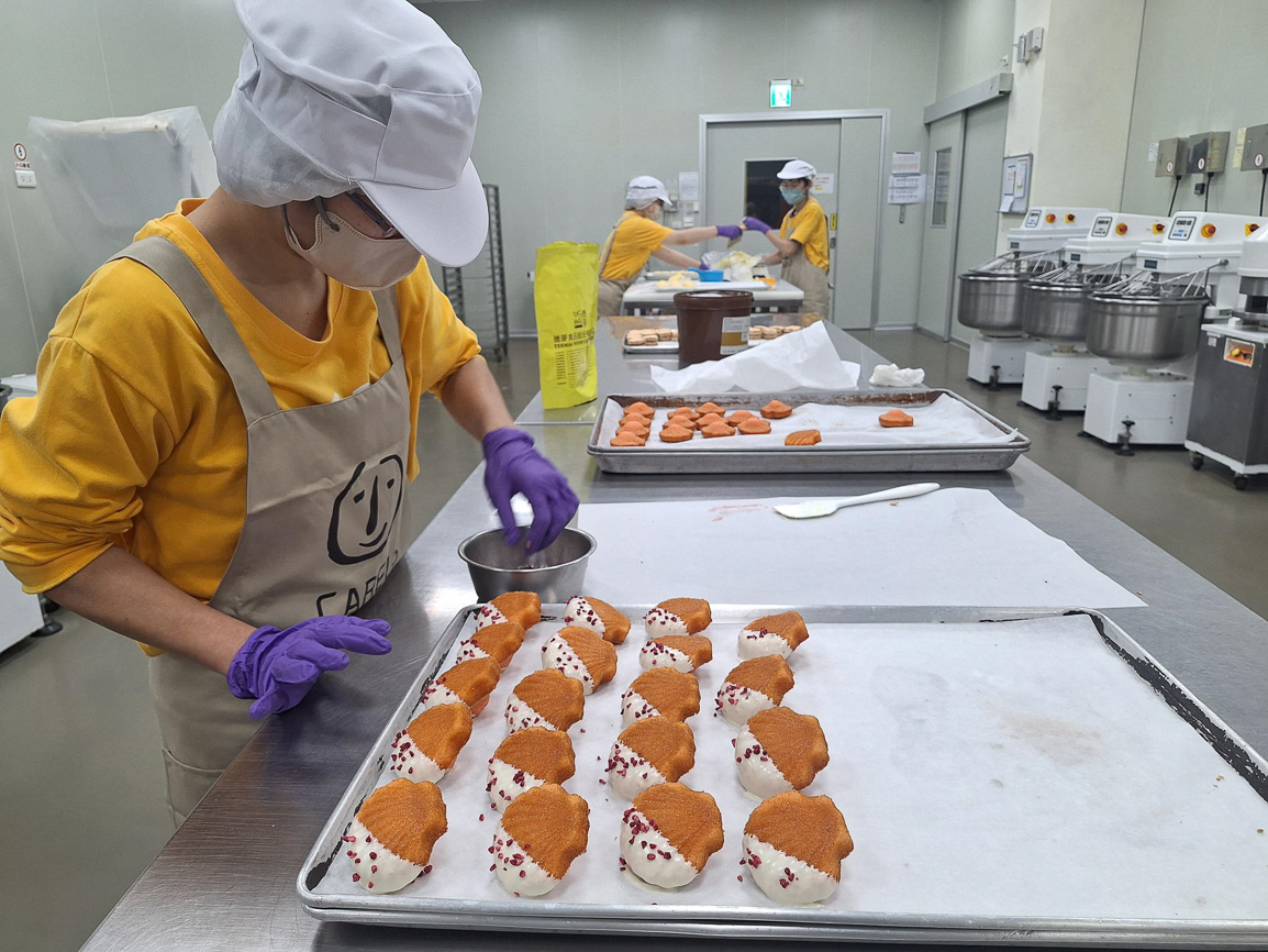 ▲憨兒正在製作貝殼造型瑪德蓮，沾上白巧克力醬後撒上莓果粒，多重工序豐富味蕾。（圖/喜憨兒喜歡你購物網提供）